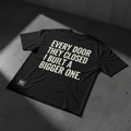 Black heavyweight tee with bold white typography - Every Door They Closed I Built A Bigger One
